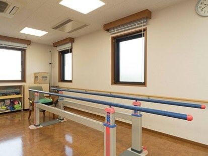 平行棒のそばにはいすが置かれ、窓の下の棚にはたくさんの用具が収納されている。