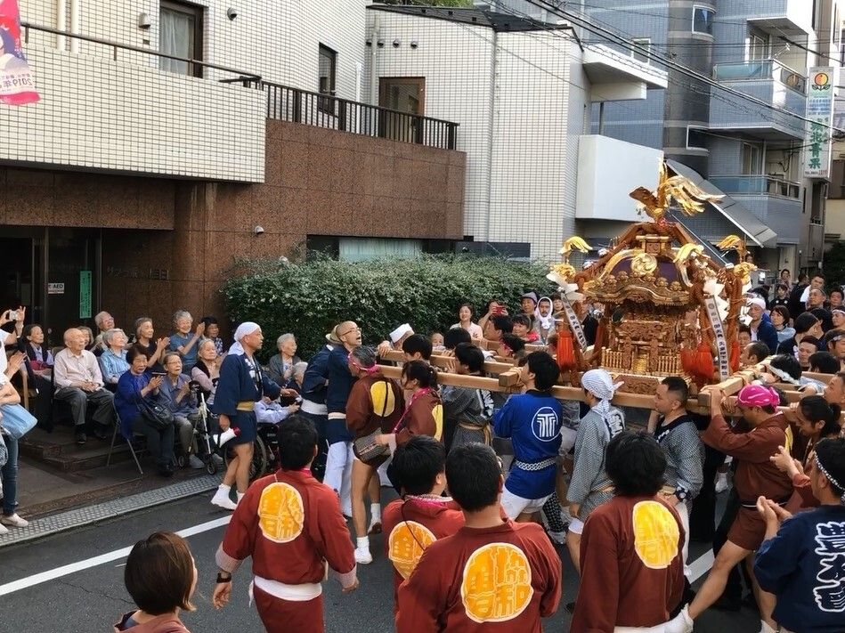 青やエンジのハッピを着た男性たちが神輿を担ぎ、ホームの前でお披露目をしていて、入居者たちが見ている。