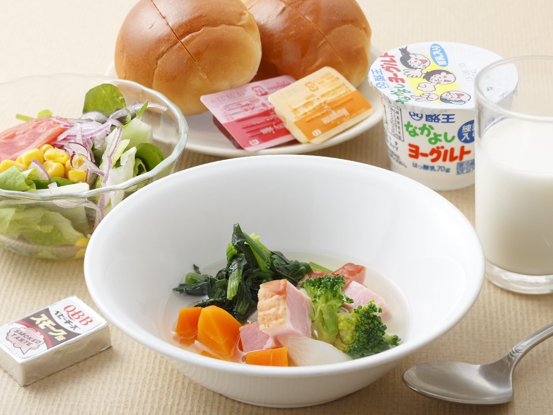 ベーコンと野菜のスープに、ロールパン、ジャムやマーガリン、牛乳、サラダなどが並べられている。