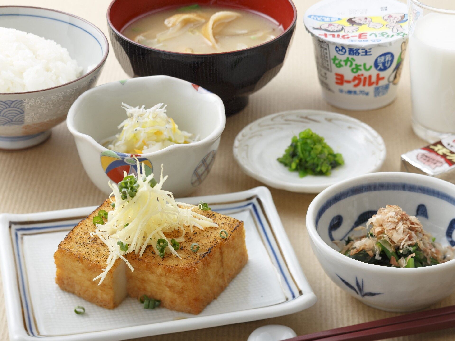 白いご飯に味噌汁、ほうれん草のお浸しに厚揚げ、牛乳、ヨーグルト、野菜の小鉢などが並べられている。