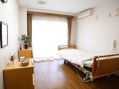 寝具付きのベッドやエアコン、タンスなどが置かれた部屋。大きな窓にはカーテンが付き、明るい雰囲気。