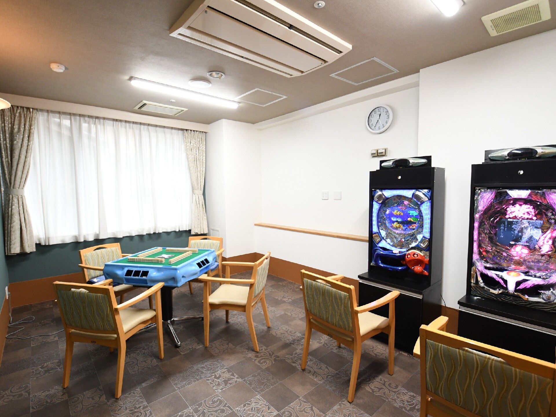 麻雀卓やパチンコ台が置かれた部屋。キラキラと光る種類の異なるパチンコ台が2台置かれ、窓も付いている。