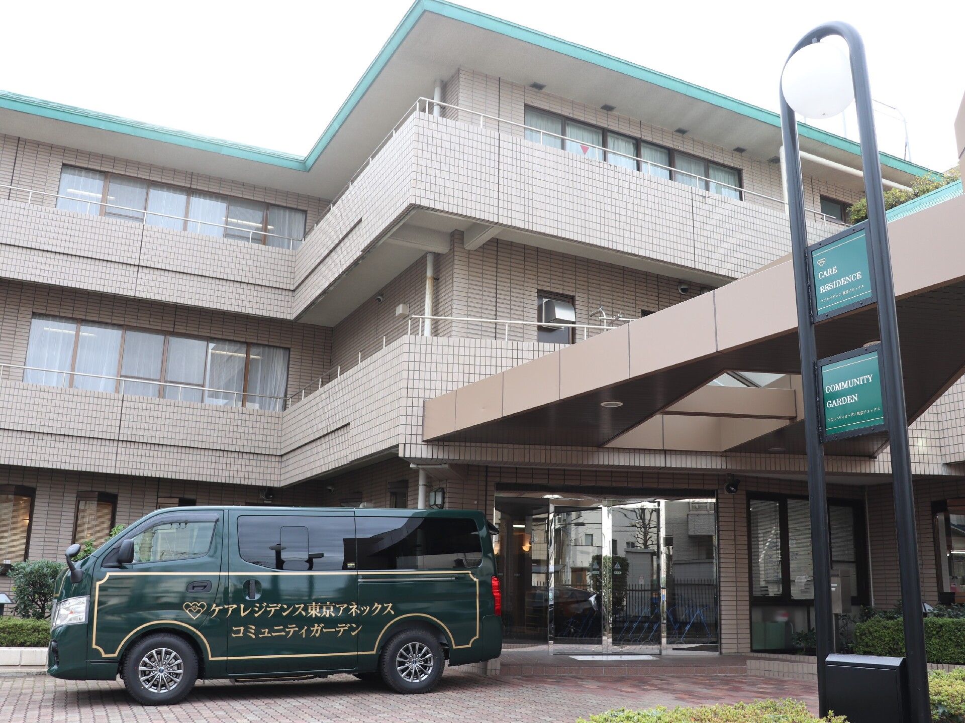 ブラウン系の3階建ての建物は玄関に車寄せが付き、ホーム名が書かれたダークグリーンのシャトルが止まっている。
