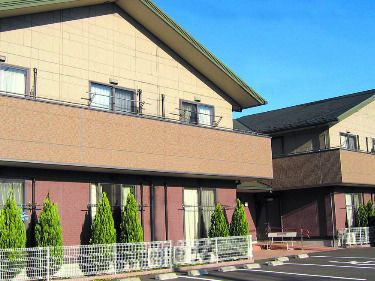 三角屋根やベランダが付いたブラウン系の２階建ての建物は日当たり良好で２棟あり、周りには草木が植えられている。
