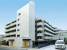 白を基調とした6階建ての大きな建物が建っている敷地内には駐車場があり、ホームの白いバンが止まっている。