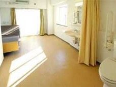 カーテンで開け閉めするタイプのトイレが設置された広い部屋には介護ベッドや大きな窓がある。