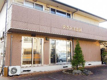 ベランダが付いた２階建ての建物はブラウン系の外壁で、外壁にはホーム名が書かれている。