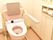 背もたれと手すりが付いたピンクの便座が付いたトイレ。操作ボタンは壁に設置されている。