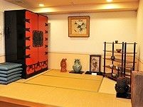 赤と黒の大きな収納家具が置かれた畳のスペースにはつぼや座布団などもある。
