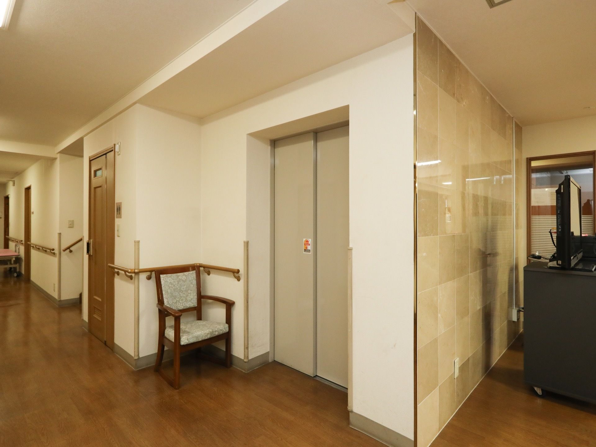 施設館内に完備されたエレベーターである。そばには椅子が1脚配備され、壁の角には衝撃緩和材が装着されている。