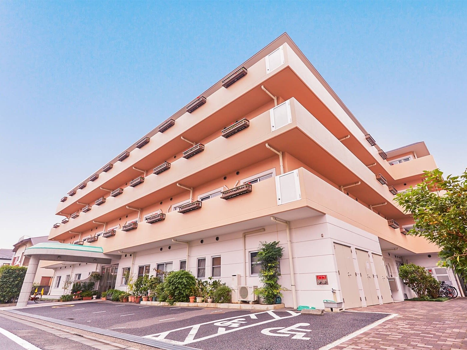 3階建ての建物はすっきりとしたスタイリッシュな外観で、玄関のそばに駐車場があり、周辺には緑も多くある。