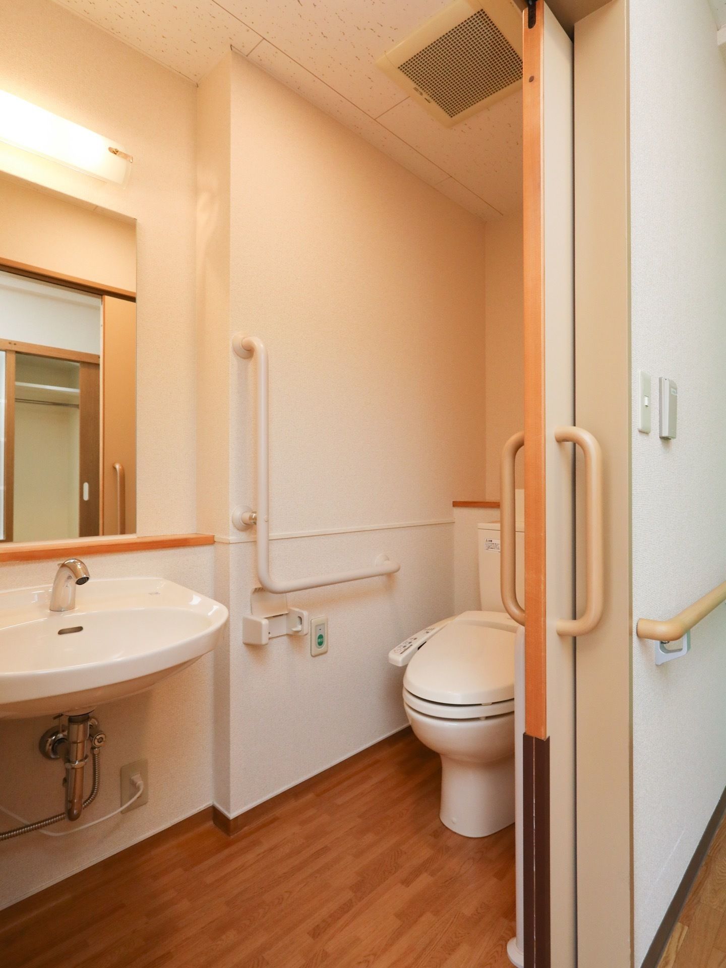 トイレ個室内に温水洗浄式便座が設置されており、座って右手にＬ字の手すりと緊急呼び出しボタンが取り付けられている。
