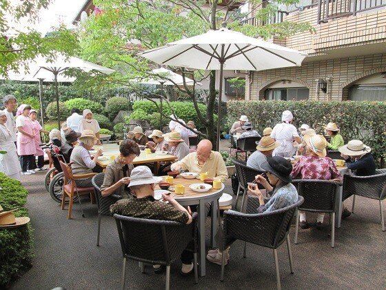 緑の多い敷地内にはパラソル付きのテーブルセットがたくさん置かれ、入居者が外で食事を楽しんでいる。