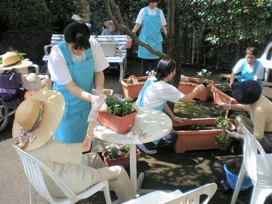 プランターに花の苗を植えている入居者とサポートに当たっているスタッフたち。屋外の活動で入居者は帽子をかぶっている。
