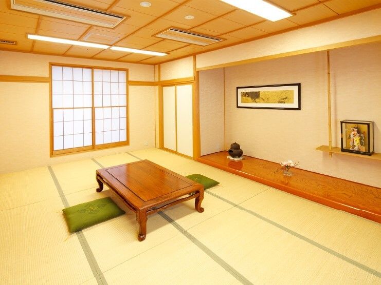 障子が窓に設置され、畳が敷かれた和室。日本人形や花が飾られ、テーブルの周りには座布団が敷かれている。
