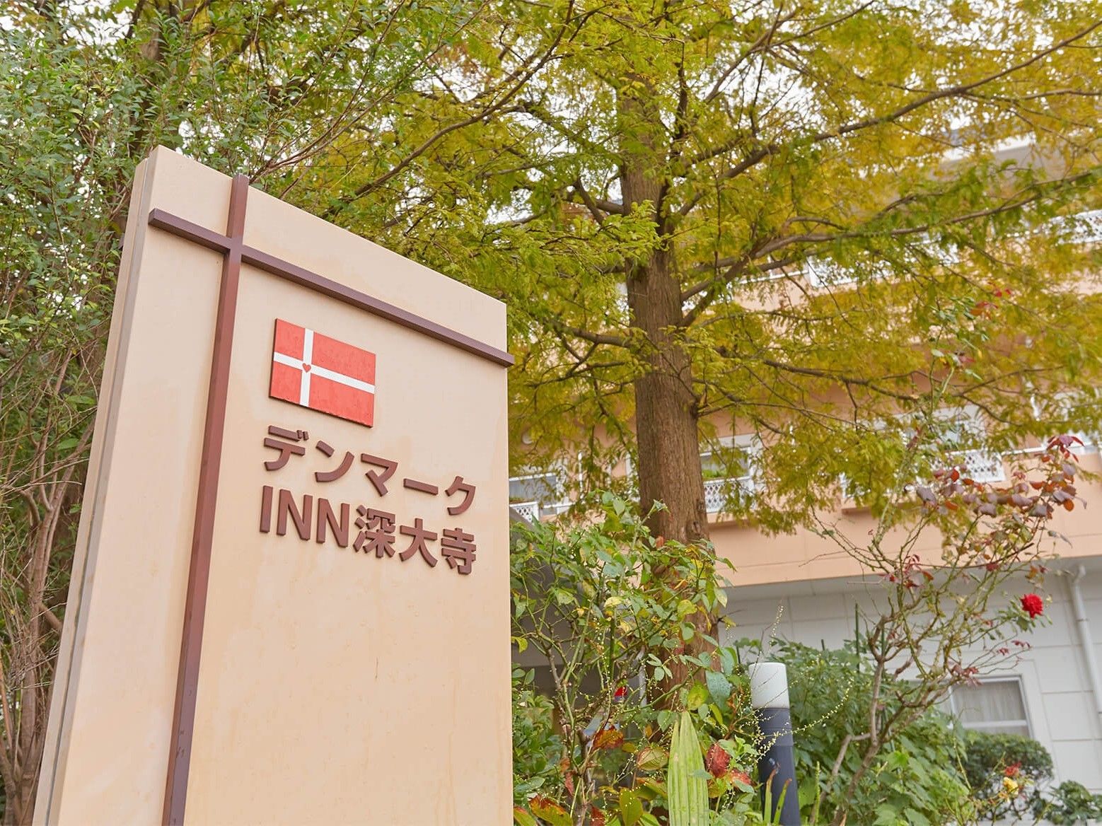 緑の多い敷地内に立つベージュと白の建物。出入り口にはホーム名が大きく書かれた門がある。