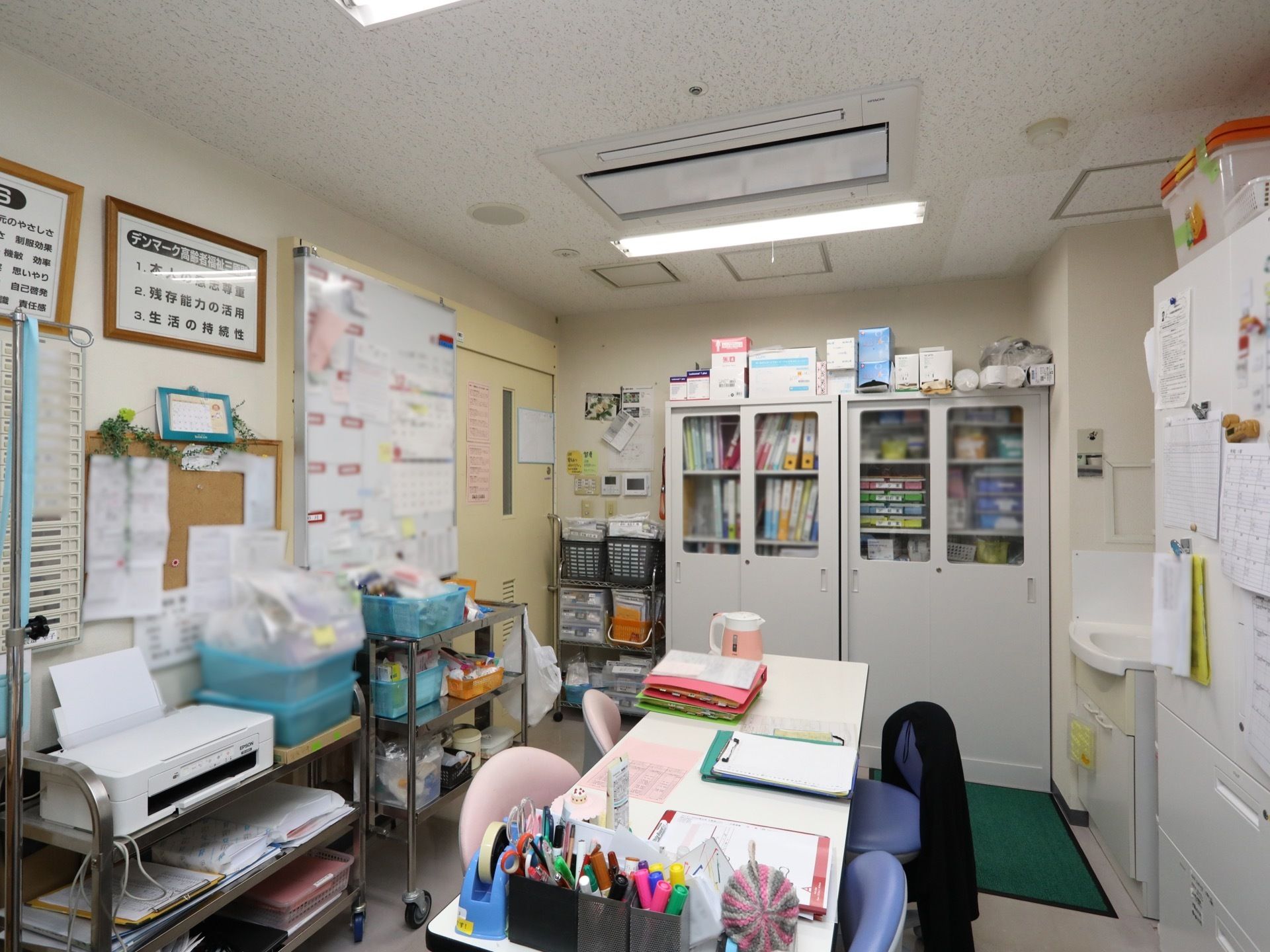 書類棚や机が置かれた部屋がある。壁には大きなホワイトボードやコルクボード、行動理念などが書かれた額縁が掛けられている。