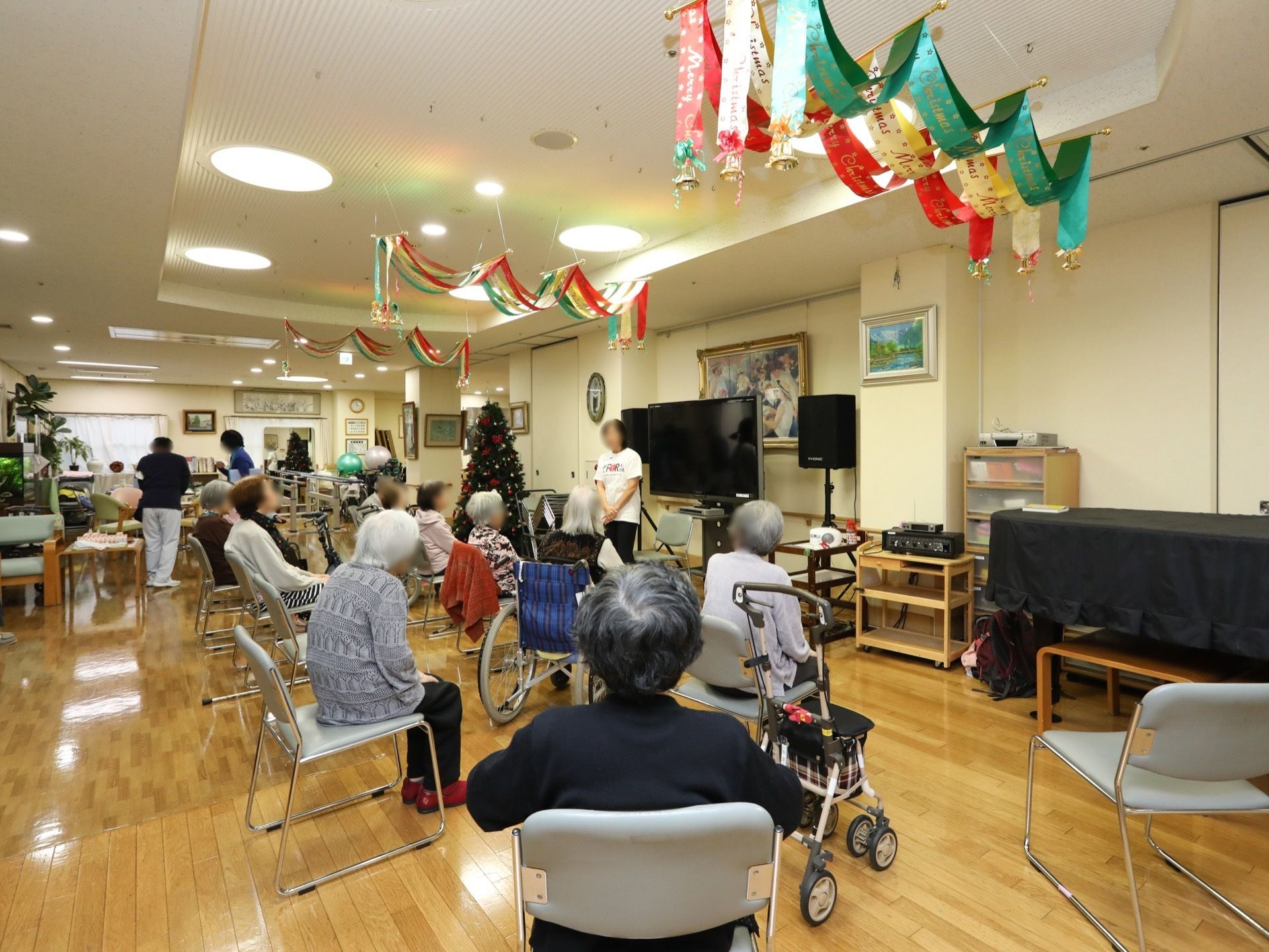 フローリングの広いホールがある。入居者様が10名ほど集まって椅子に座り、スタッフの話に耳を傾けている。