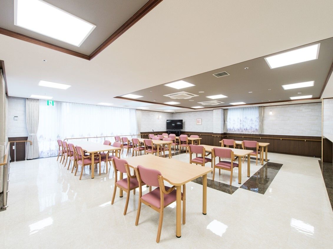 ピンクの椅子がセットされた木製のテーブルセットが多く置かれた食堂。テレビも設置されている。