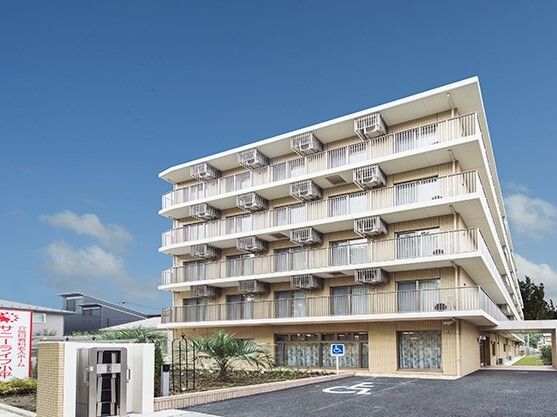 ５階建ての建物が建つ敷地内には駐車場があり、草木が植えられているスペースもある。