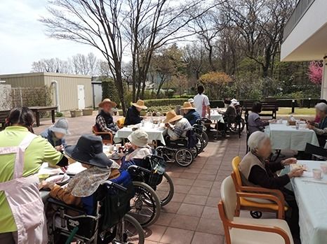 花の咲く道を散歩する車椅子に乗った高齢女性と介助をするヘルパー