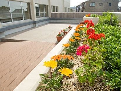 赤や黄色の花が植えられた花壇が設置されたウッドデッキのテラス。プランターも置かれている。