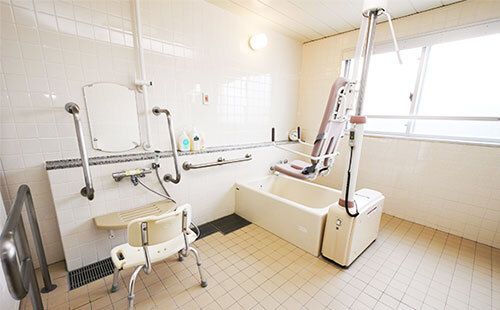 シャワーやシャワーチェア、リフトが設置された浴室は清潔感があり、白でまとめられている。大きな窓が付き明るい雰囲気。