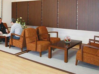 ブラウン系の応接セットが複数置かれたロビーには花や観葉植物が飾られ、男性が二人座っている。