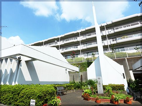 白い塔のような建物が右側にあり、左側には少し大きな白い建物があり、奥には施設らしき建物が建っている。