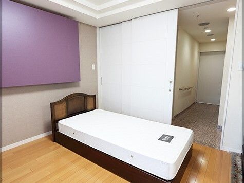 マットレス付きのベッドが置かれたフローリングの部屋。玄関からはまっすぐな廊下が伸びている。