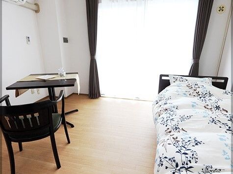 寝具付きのベッドやテーブルセットが置かれたフローリングの部屋は日当たりがよく、大きな窓が付いている。