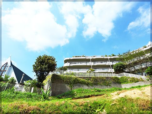 青い空の下に建っている白い大きな建物。各フロアにベランダがあり、横に長い。その横には教会がある。