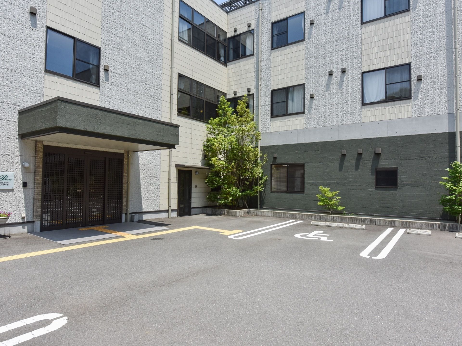 施設の入り口には大きなひさしが設けられている。施設の周囲にはレンガで区切られた花壇用のスペースがあり木々が植えられている。