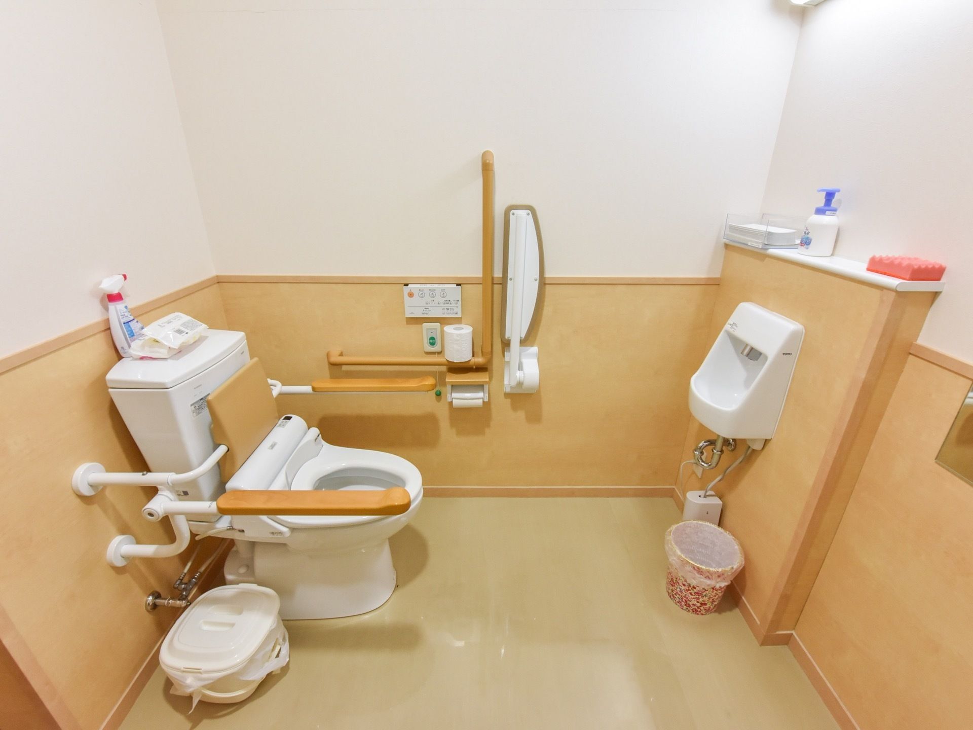 トイレは温水洗浄便座である。左側の壁に縦と横の手すりがある。手洗い場の下に小さめのゴミ箱が用意されている。