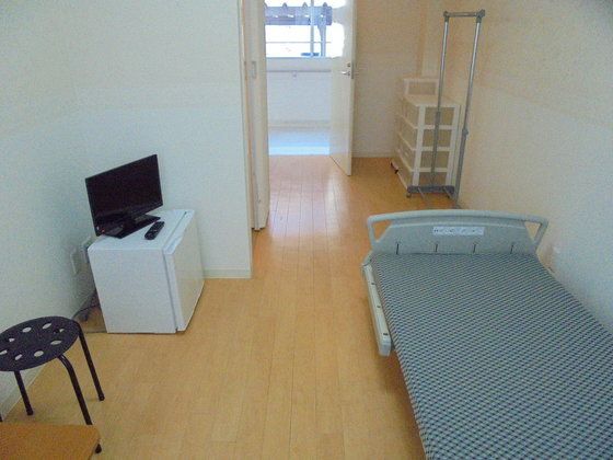 ミニ冷蔵庫の上にテレビを置き、衣類かけや収納を備えた部屋