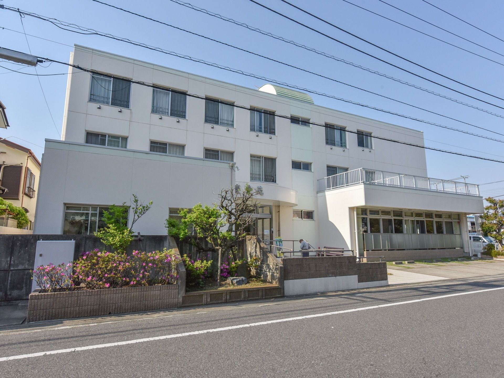 白い外観の３階建ての施設である。周囲はブロック塀と木が植えられている。近隣にはスーパーや病院など便利な施設が揃っている。