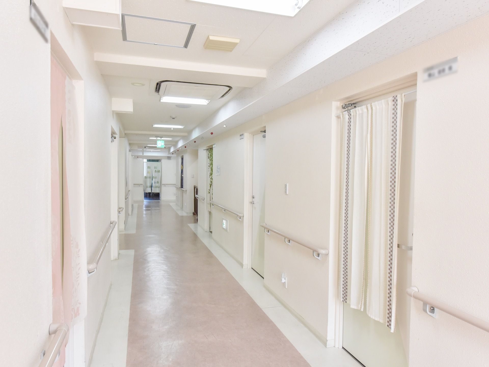 廊下の壁や居室扉、手すりは白で統一されて爽やかな印象を与えてくれる。居室には入居者様の名前が貼られている。
