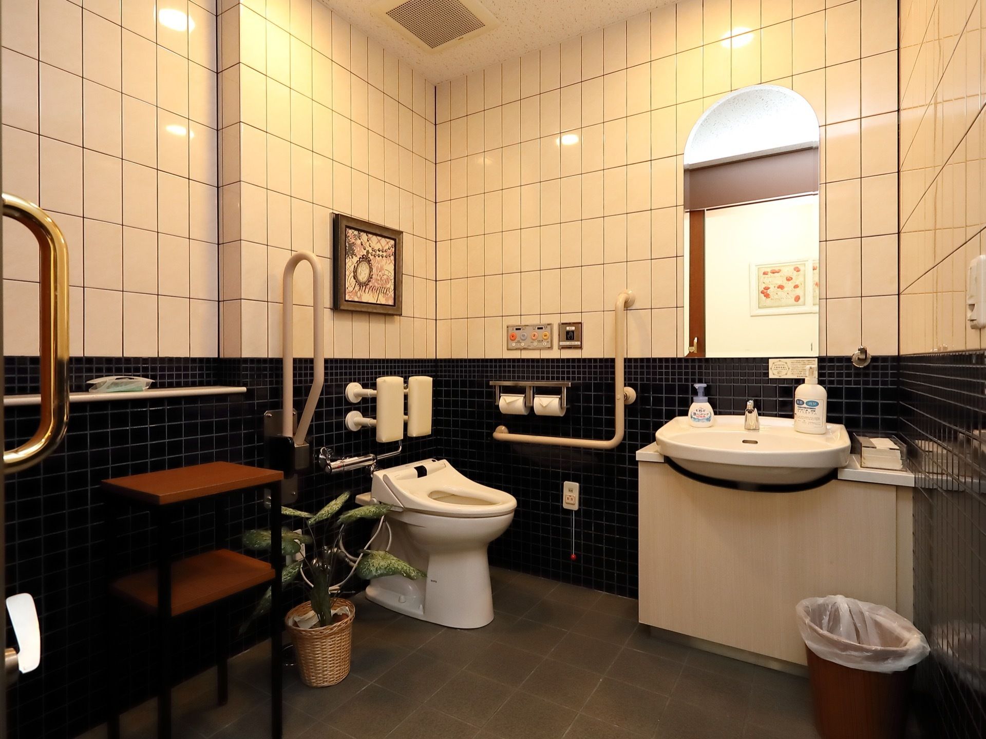 白と黒のタイルが貼られた壁に絵画が飾られた、華やかでおしゃれなトイレである。安全性のために手すりと、緊急ボタンが設置されている。