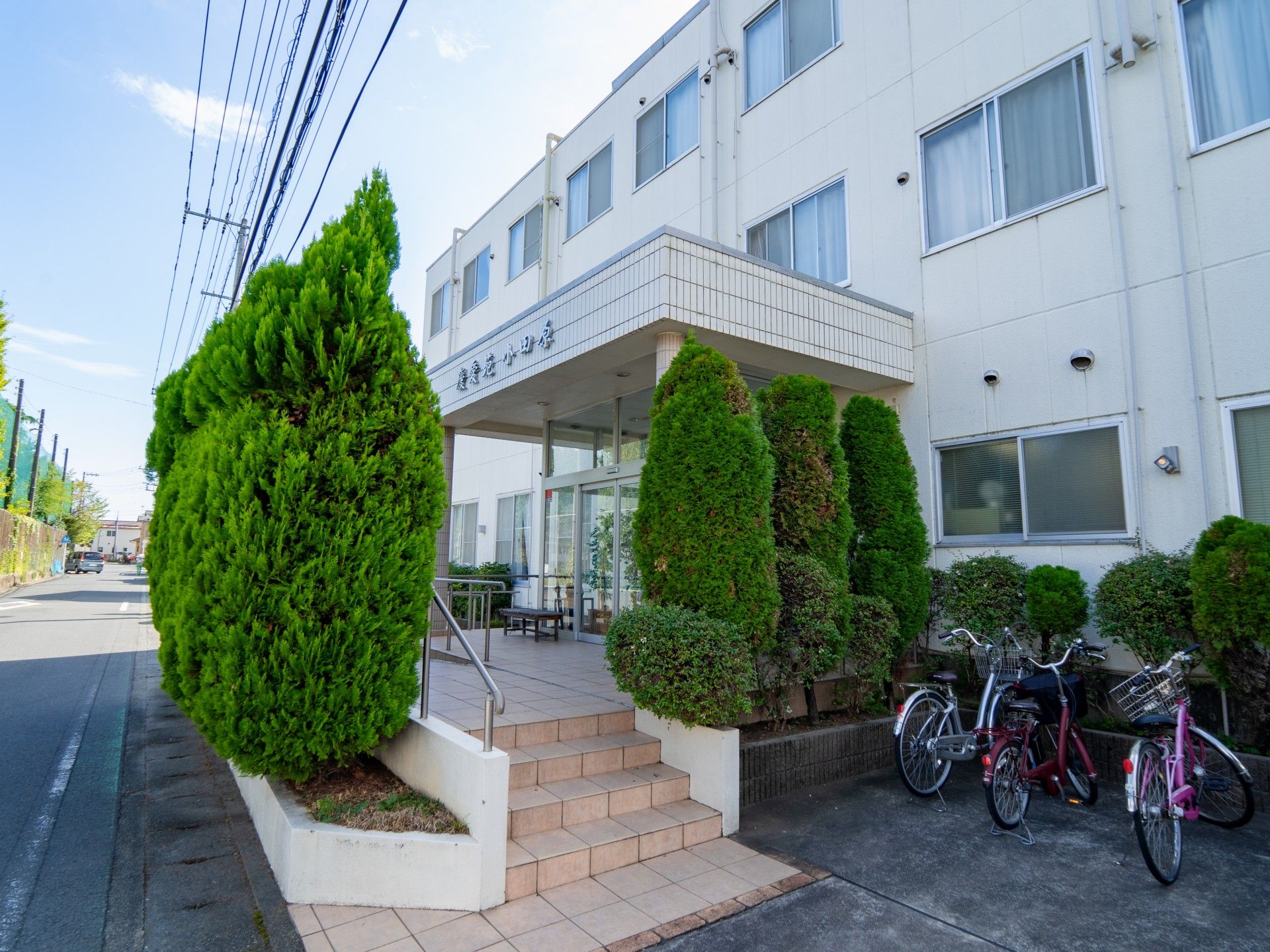 白い3階建ての建物は日当たりのいい場所にあり、敷地内には駐輪場と駐車場がある。