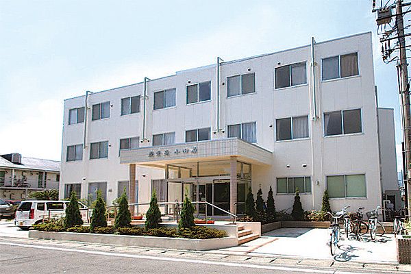 駐車場や駐輪場が付いた敷地内には白い3階建ての建物があり、玄関には手すり付きのスロープと階段が付いている。