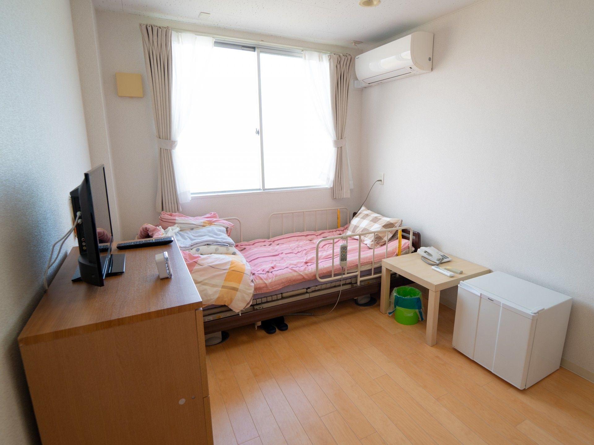 窓辺に介護用ベッドを置き、チェストや冷蔵庫などの家具を配置した部屋
