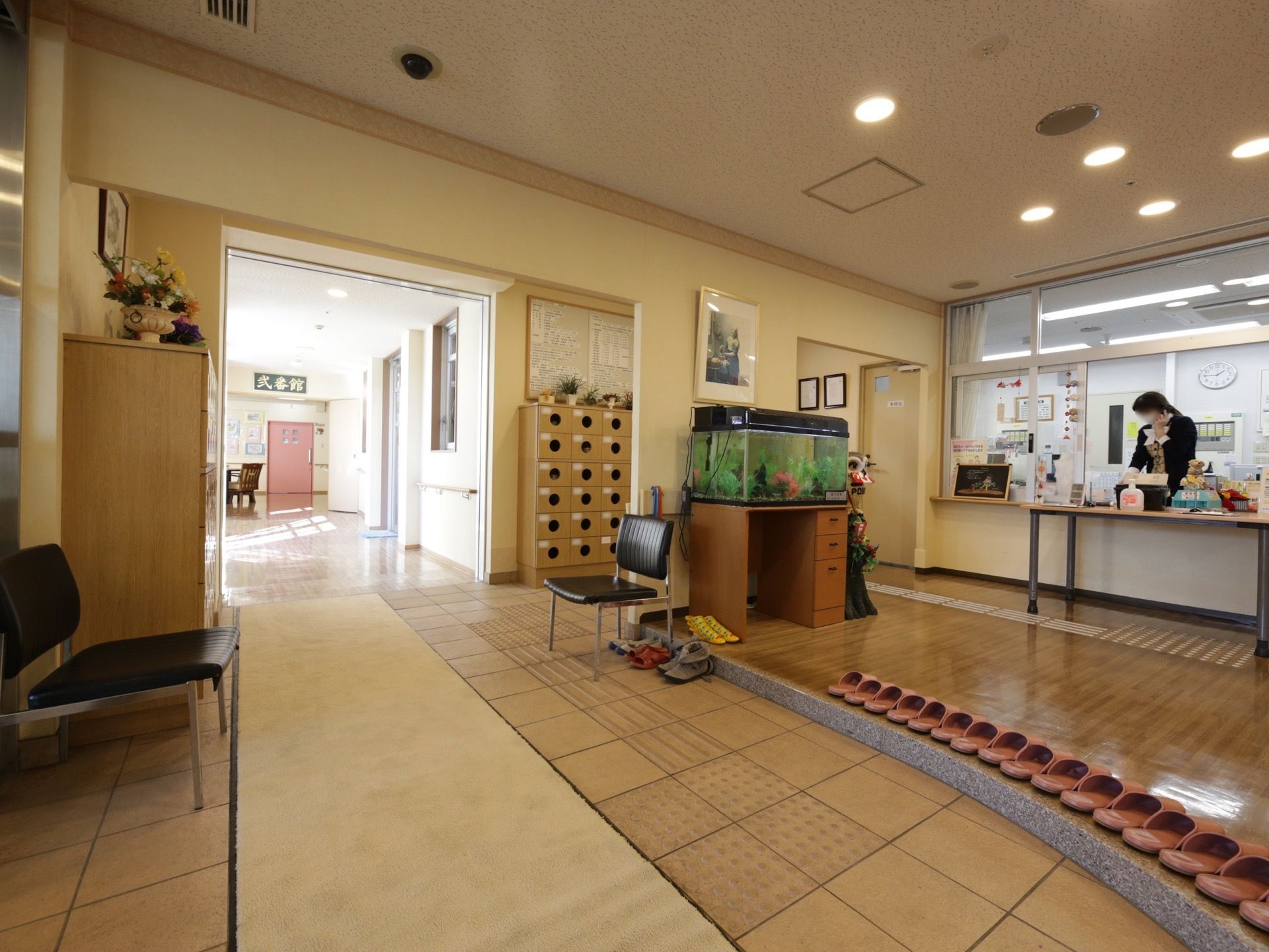 正面に受付のカウンターがある広い玄関。スリッパが一列に並べられており、奥にはスロープが設けられている。