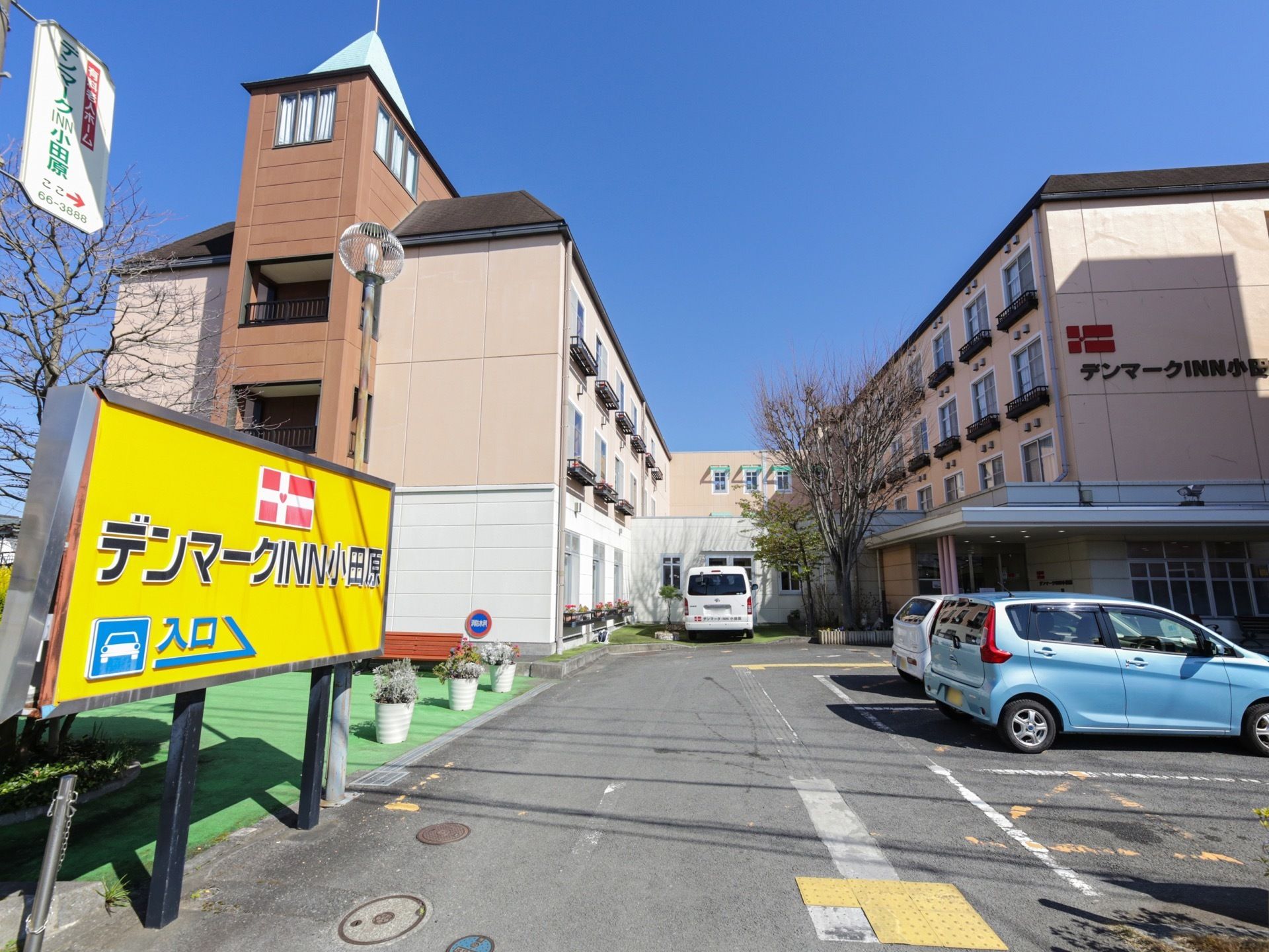 アスファルトで舗装された広い敷地に、施設の建物が建っている。手前は駐車スペースになっており、車が数台停まっている。