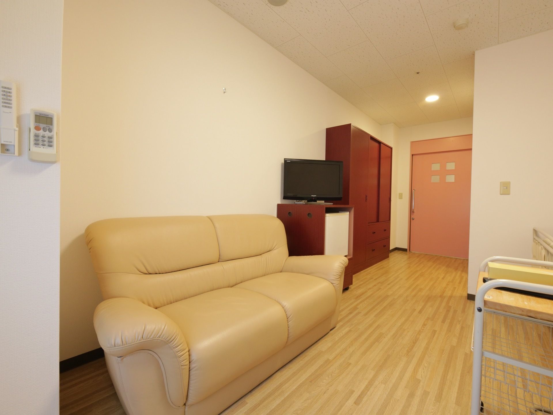 明るい木目調で、あたたかみがある床の居室。介護用ベッドのほか、ソファや冷蔵庫、テレビ、タンスなどが置かれている。