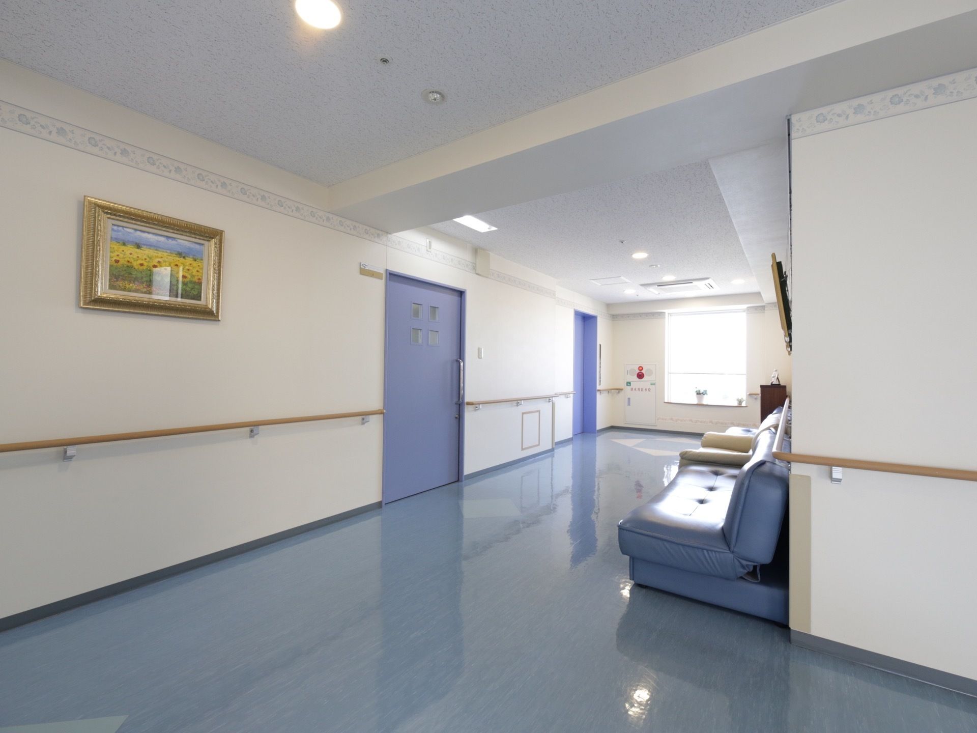薄いブルーを基調とした廊下がある。壁には手すりが備え付けられており、白や水色のソファが置かれている。