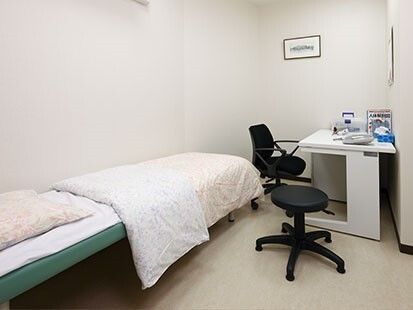 寝具がセットされたベッドが左にあり、右側には診察用の椅子と椅子の座る椅子、デスクがある。