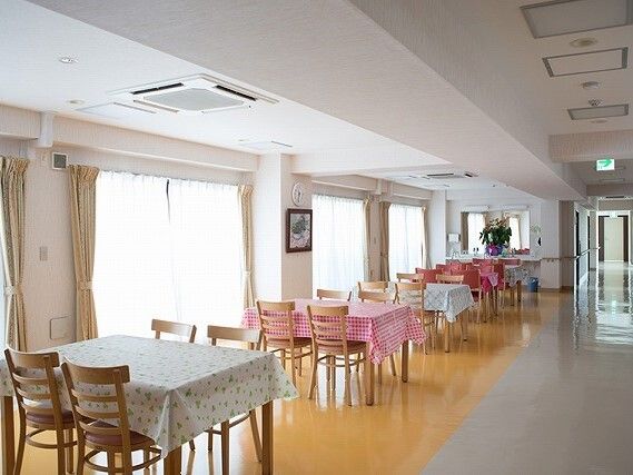 大きな窓が付いた食堂にはテーブルクロスがセットされたダイニングテーブルが複数置かれ、観葉植物が飾られている。