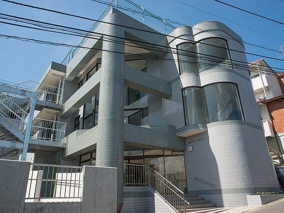 日当たりのいい場所に建っている4階建ての建物はグレー系の外観。玄関先には手すり付きの階段もある。