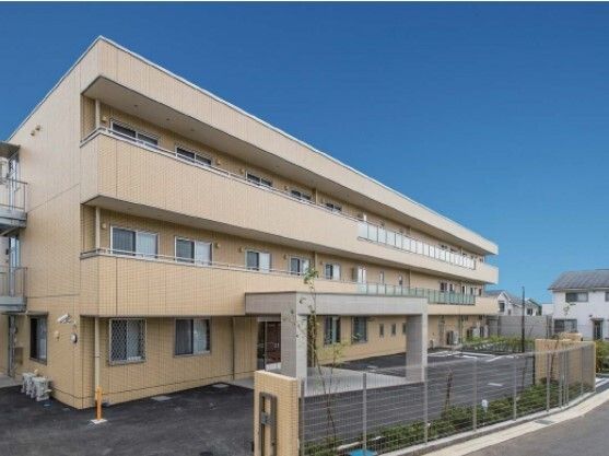ブラウン系の３階建ての建物は玄関に車寄せがあり、敷地内には駐車場がある。