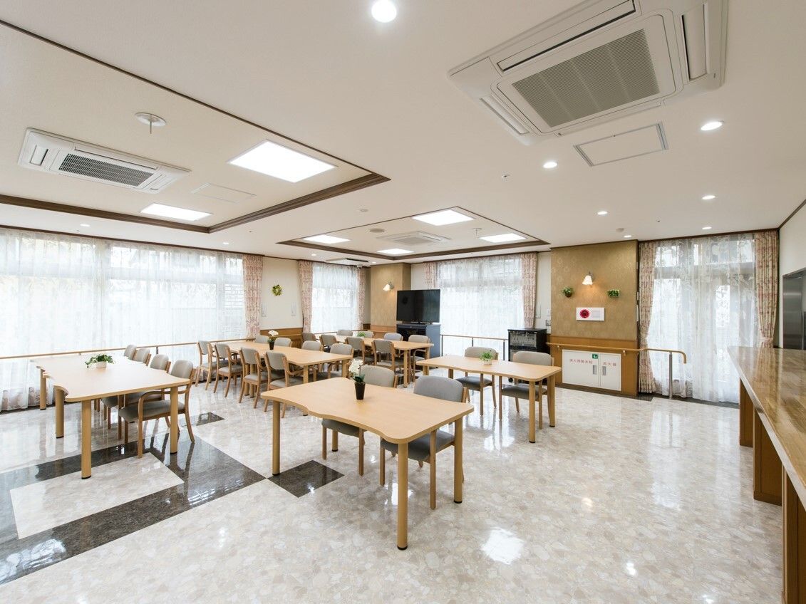 テレビや複数のダイニングテーブルセットが置かれた食堂。大きな窓がたくさんあり、明るい雰囲気。